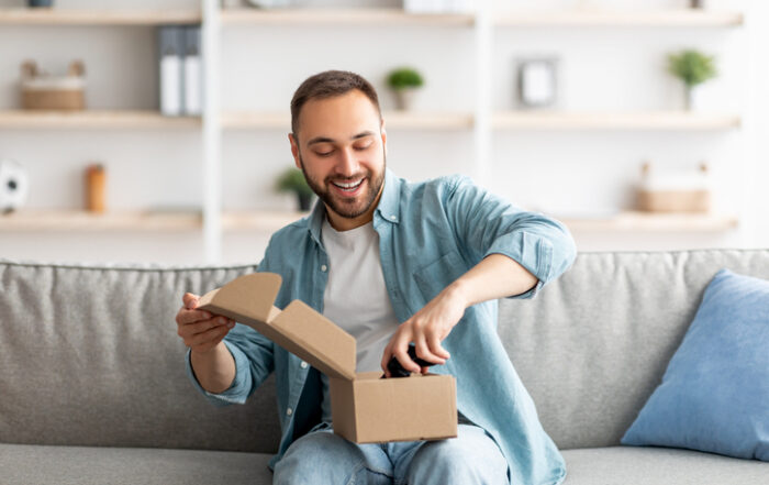 Happy Caucasian man receiving package unboxing parcel taking out gaming joystick sitting on sofa in living roomQuick Reliable Printing (QRP)