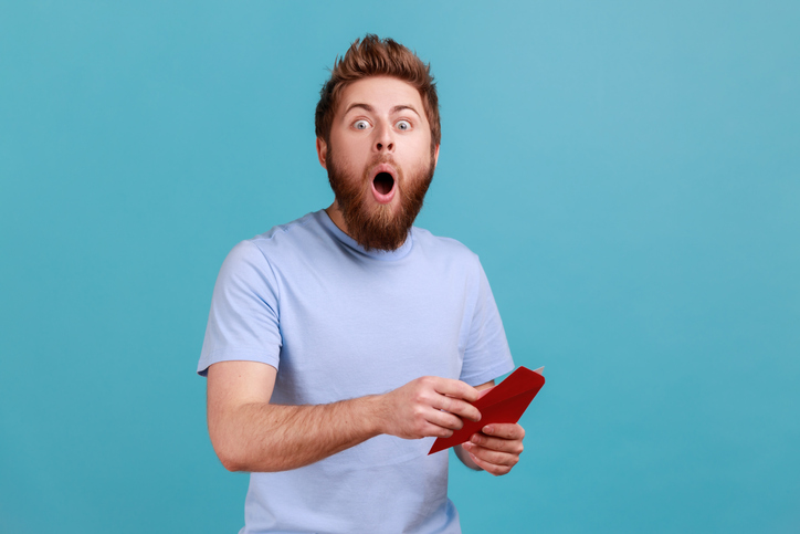 Man in T-shirt reading letter or greeting card holding envelope being astonished of shocked news | Quick Reliable Printing (QRP) Quick Reliable Printing (QRP)