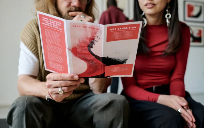 Two people sit together reading a red-and-white art brochure.Quick Reliable Printing (QRP)