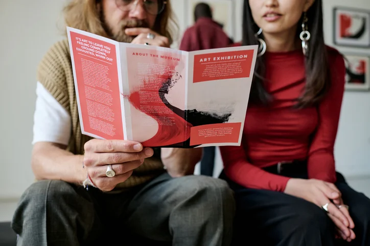 Two people sit together reading a red-and-white art brochure.Quick Reliable Printing (QRP)