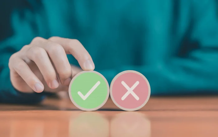 Close-up of a hand placing green checkmark and red X tiles on a wooden surface, symbolizing correct vs. incorrect choices.Quick Reliable Printing (QRP)
