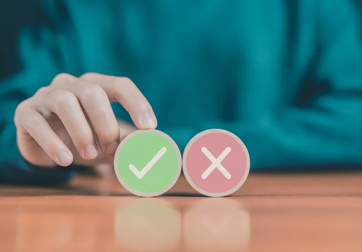 Close-up of a hand placing green checkmark and red X tiles on a wooden surface, symbolizing correct vs. incorrect choices.Quick Reliable Printing (QRP)