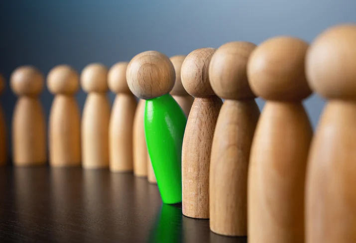 Line of wooden figures with one bright green figure standing out from the grayscale crowd, symbolizing individuality or standing out from the group.Quick Reliable Printing (QRP)